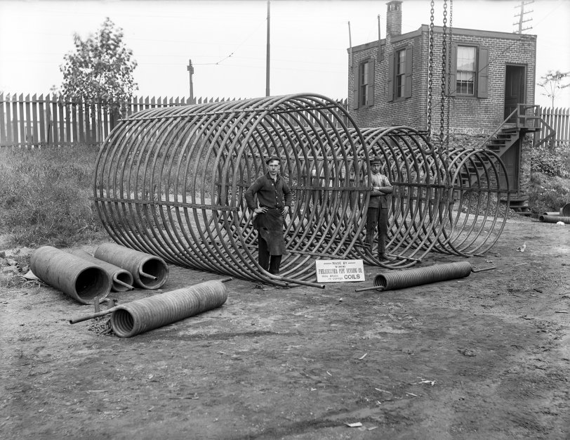 Boys & Coils: 1910s The Philadelphia Pipe Bending Company, founded in 1880, is still in operation today. Here we see two workers standing inside some large coils with advertising signage. 6½ x 8½ inch glass negative. View full size.