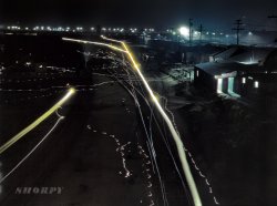 March 1943. Another night shot by Jack Delano, taken on his Santa Fe rail trip west from Chicago in 1943. His description of this scene: "Activity in the Santa Fe R.R. yard, Los Angeles. Due to blackout regulations, floodlights, switch lights, locomotive headlights and lights on the bridge in background have been shaded to cast light downward. Broad streaks of light are caused by paths of locomotive headlights, thin wavy lines by lamps of switchmen working in the yard." 4x5 Kodachrome transparency by Jack Delano. View full size.