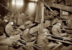 January 1911. South Pittston, Pennsylvania. "A view of the Pennsylvania Breaker. 'Breaker boys' remove rocks and other debris from the coal by hand as it passes beneath them. The dust is so dense at times as to obscure the view and penetrates the utmost recesses of the boys' lungs." Photo by Lewis Wickes Hine. View full size.

From the 1906 book The Bitter Cry of the Children by labor reformer John Spargo:

&nbsp; &nbsp; &nbsp; &nbsp; Work in the coal breakers is exceedingly hard and dangerous. Crouched over the chutes, the boys sit hour after hour, picking out the pieces of slate and other refuse from the coal as it rushes past to the washers. From the cramped position they have to assume, most of them become more or less deformed and bent-backed like old men. When a boy has been working for some time and begins to get round-shouldered, his fellows say that &#8220;He&#8217;s got his boy to carry round wherever he goes.&#8221;  &nbsp; &nbsp; &nbsp; &nbsp; The coal is hard, and accidents to the hands, such as cut, broken, or crushed fingers, are common among the boys. Sometimes there is a worse accident: a terrified shriek is heard, and a boy is mangled and torn in the machinery, or disappears in the chute to be picked out later smothered and dead. Clouds of dust fill the breakers and are inhaled by the boys, laying the foundations for asthma and miners&#8217; consumption.

&nbsp; &nbsp; &nbsp; &nbsp; I once stood in a breaker for half an hour and tried to do the work a 12-year-old boy was doing day after day, for 10 hours at a stretch, for 60 cents a day. The gloom of the breaker appalled me. Outside the sun shone brightly, the air was pellucid, and the birds sang in chorus with the trees and the rivers. Within the breaker there was blackness, clouds of deadly dust enfolded everything, the harsh, grinding roar of the machinery and the ceaseless rushing of coal through the chutes filled the ears. I tried to pick out the pieces of slate from the hurrying stream of coal, often missing them; my hands were bruised and cut in a few minutes; I was covered from head to foot with coal dust, and for many hours afterwards I was expectorating some of the small particles of anthracite I had swallowed.

&nbsp; &nbsp; &nbsp; &nbsp; I could not do that work and live, but there were boys of 10 and 12 years of age doing it for 50 and 60 cents a day. Some of them had never been inside of a school; few of them could read a child&#8217;s primer. True, some of them attended the night schools, but after working 10 hours in the breaker the educational results from attending school were practically nil. &#8220;We goes fer a good time, an&#8217; we keeps de guys wot&#8217;s dere hoppin&#8217; all de time,&#8221; said little Owen Jones, whose work I had been trying to do.

&nbsp; &nbsp; &nbsp; &nbsp; From the breakers the boys graduate to the mine depths, where they become door tenders, switch boys, or mule drivers. Here, far below the surface, work is still more dangerous. At 14 or 15 the boys assume the same risks as the men, and are surrounded by the same perils. Nor is it in Pennsylvania only that these conditions exist. In the bituminous mines of West Virginia, boys of 9 or 10 are frequently employed. I met one little fellow 10 years old in Mount Carbon, West Virginia, last year, who was employed as a &#8220;trap boy.&#8221; Think of what it means to be a trap boy at 10 years of age. It means to sit alone in a dark mine passage hour after hour, with no human soul near; to see no living creature except the mules as they pass with their loads, or a rat or two seeking to share one&#8217;s meal; to stand in water or mud that covers the ankles, chilled to the marrow by the cold draughts that rush in when you open the trap door for the mules to pass through; to work for 14 hours &#8212; waiting &#8212; opening and shutting a door &#8212; then waiting again for 60 cents; to reach the surface when all is wrapped in the mantle of night, and to fall to the earth exhausted and have to be carried away to the nearest &#8220;shack&#8221; to be revived before it is possible to walk to the farther shack called &#8220;home.&#8221;

&nbsp; &nbsp; &nbsp; &nbsp; Boys 12 years of age may be legally employed in the mines of West Virginia, by day or by night, and for as many hours as the employers care to make them toil or their bodies will stand the strain. Where the disregard of child life is such that this may be done openly and with legal sanction, it is easy to believe what miners have again and again told me &#8212; that there are hundreds of little boys of 9 and 10 years of age employed in the coal mines of this state.
-- John Spargo, The Bitter Cry of the Children (New York: Macmillan, 1906)