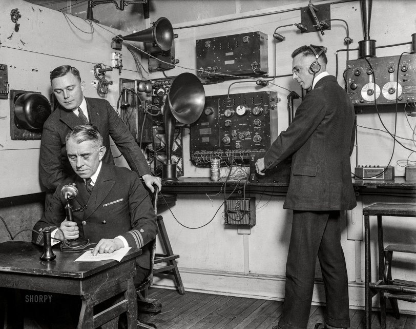 Ahoy, Mateys: 1923 January/February 1923. "Headquarters of the U.S. Coast Guard are using a unique method for distributing news of their service by means of radio. Capt. F.C. Billard, aide to the commandant, is shown broadcasting. Lt. F.A Zensler is coaching him from the receiving set, which is being used by Lt. E.M. Webster (with earpieces)." Harris & Ewing glass negative. View full size.