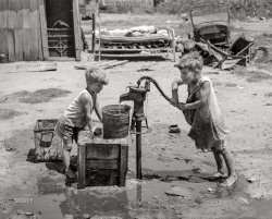 July 1939. "Children of May Avenue camp pumping water from thirty-foot well which supplies about a dozen families. Oklahoma City, Oklahoma." Photo by Russell Lee. View full size.

&nbsp; &nbsp; &nbsp; &nbsp; General caption: Photographs show exterior and interior of shacks, tents, other makeshift shelter in May Avenue camp, which is partially under bridge and adjacent to city dump and hog wallow. Squalor, filth, vermin in which poverty-stricken inhabitants dwell. Water supplied by shallow wells and water peddler. Piles of rubbish and debris in which children and adults have injured feet. Privies. Families eating food from vegetable dumps, packing houses and discarded from hospital. Children clothed in gunny sacks. Malnourished babies. Sick people. Cooking, washing, ironing, patching. Improvised chicken coop. Corn patch."