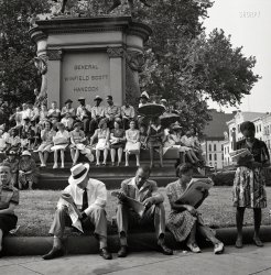 July 1943. Washington, D.C. "Waiting for the parade to recruit civilian defense volunteers." Entertaining themselves with the hand-held device known as a "newspaper." Photo by Esther Bubley, Office of War Information. View full size.