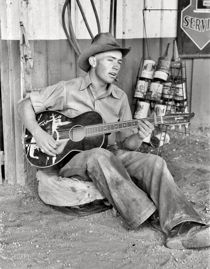 The Texaco Troubadour: 1940 June 1940. Pie Town, New Mexico. "Farm boy playing guitar in front of the filling station and garage." 35mm nitrate negative by Russell Lee. View full size.